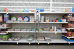 A metal retail shelf cart hanging on a store aisle shelf, surrounded by colorful party supplies, plates, cups, napkins, and packaged goods.