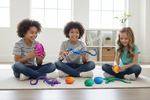 Three children sitting on a rug in a bright room, each holding a colorful textured toy while other colorful toys are scattered on the floor. A large semi-transparent watermark reading 'Dallas General Wholesale' is overlaid across the center.