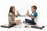 Two children sitting on the floor playing with small wrestling figure toys and accessories, with product boxes placed beside them on a white studio background. A large 'Dallas General Wholesale' watermark is overlaid across the center.