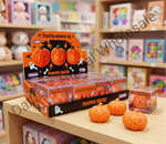 A retail display box and individual boxes of Crunchy Squeeze Toy 'Pumpkin Squish' on a wooden shelf, with three small carved orange pumpkin squeeze toys placed in front. The background shows a softly blurred toy store interior with shelves and colorful items.