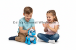 A young boy in a light blue t-shirt and tan pants sits on the floor smiling next to a girl in a pink t-shirt and blue jeans who is clapping her hands, both looking at a small blue and white robotic dog toy on a white background. A watermark reading 'Dallas General Wholesale' is overlaid across the center.
