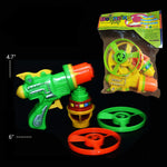 A toy set labeled 'Bouncing Top' shown on a black background, including a green and orange toy gun, a packaged set of spinning tops, a green top, and an orange top. Product text and dimensions are printed on the left side.