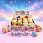 A display box of 'Mystery Squishy Steameo Bun' toys with several colorful round squishy balls and bun-shaped containers arranged in front on a pink surface against a starry pastel galaxy background.