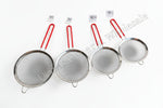 Set of four metal strainers with red handles on a white background