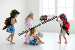 Four children wearing colorful dinosaur and unicorn costume hoodies play in a bright white room. The costumes include green, red, black, and pastel rainbow designs.