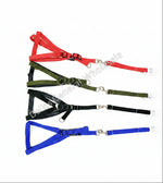 Four pet harnesses with matching lead straps laid out on a light beige tiled floor. The harnesses come in red, olive green, black, and blue, each with a white plastic end cap.