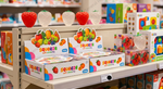 A retail store shelf displaying ASMA 'squeeze soft stretchy' toys in white boxes with colorful fruit illustrations, alongside translucent and red strawberry-shaped items on top.