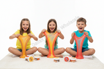 Three children sitting cross-legged on a white carpet, stretching colorful slime in front of them. Small containers of the product are placed on the floor in front of each child.
