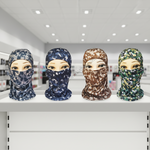 Four full-face balaclavas displayed on mannequin heads in a retail store setting, shown in four camouflage patterns: blue digital camo, navy digital camo, brown digital camo, and green digital camo.