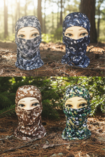 Three camouflage balaclava face masks displayed on mannequin heads in an outdoor forest setting. The top row shows a gray and white digital camo pattern, and the bottom row shows brown, beige, and green digital camo patterns.