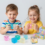 Two children smiling and playing with translucent squishy toy cubes on a white table, with product boxes visible on the right. The scene is brightly lit against a light gray background.