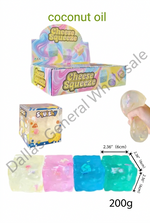 Coconut oil-based 'Cheese Squeeze' squishy toys shown in a retail display box, a smaller display box, a hand holding a translucent squishy, a row of four colorful squishys (yellow, pink, blue, teal), and dimension labels on a white background with 'coconut oil' and '200g' text.