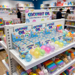 A retail display shelf showcasing 'Coconut Oil' fluid stress balls in various pastel colors, alongside other colorful toys in a toy store.