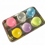 Six translucent gel-like balls in pink, blue, yellow, purple, and clear, arranged on a metal tray with large overlaid Chinese text at the top.