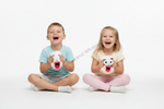 Two children sitting cross-legged on a white studio background, laughing while holding plush crying toy faces. A faint diagonal watermark is visible across the center.