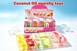 A display box and several rectangular translucent ice squishy toys in different fruit flavors, including yellow, strawberry, watermelon, and pink, arranged on a light blue gradient background with the text 'Coconut Oil squishy toys' at the top.