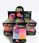 A retail display box filled with multiple individual packages of CUBE SQUEEZE BALL toys. The front package is open to show several colorful squishy cube balls inside clear plastic windows, while the display back board shows more units and the brand logo.