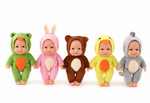 Five plush baby dolls wearing animal costume hoodies are lined up against a plain white background. The dolls are dressed as a frog, bunny, bear, duck, and shark, each in a different color: green, pink, brown, yellow, and gray, with orange accents on their bellies and beaks.