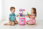 A toddler boy in a light blue shirt and a young girl in a pink polka-dot dress sit on a white floor, playing with a pink toy hospital playset. The girl holds a green toy syringe.