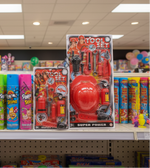 A toy set package and several colorful spray cans displayed on a store shelf. The package shows a red fire truck and a red helmet labeled 'TOY SET SUPER POWER,' while the cans include pink, blue, yellow, and green Sprinkle Star products.