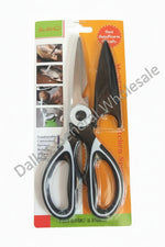 A pair of heavy-duty scissors in retail blister packaging, featuring black and silver handles with a white pivot screw, set against a gray concrete background.