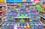 A hand holds a green squishy toy in a brightly lit toy store aisle, with multiple boxed and loose sets of cute cartoon face squishies displayed on shelves. The packaging is blue and purple, and the toys come in green, blue, yellow, pink, and purple colors.