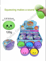 Squeezing sound sugar fidget paws in a 12-pack display box, featuring a green fidget paw that makes a sound, shown alongside other colorful options in pink, blue, purple, and yellow, with a hand demonstrating the squeezing action.