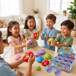 Five children are happily squeezing colorful, cartoon-face squishy toys from a box on a light wood table in a bright living room. The toys come in multiple colors including pink, red, purple, blue, green, and orange, and a retail display box is visible in the foreground.