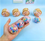 A hand holds three pastel-colored gummy bear toys with colorful bubble swirls, while four more wrapped gummy bear toys sit on a light blue background.