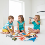 Three children sitting on a white floor playing with a variety of colorful plastic toy sea creatures, including sharks, octopus, a turtle, and a whale, in a bright, modern room.