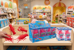 A retail display shelf in a toy store featuring Ocean Quiksy squishy plastic sea life toys, including red lobster and crab figures and blue packaging boxes. A hand is holding one of the red lobster toys on the left side of the shelf.