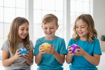 Three children sitting side by side, each holding a colorful plastic egg. The child on the left holds a blue egg with white stars, the middle child holds a yellow egg with white stars, and the child on the right holds a purple egg with white stars.