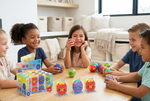 Four children sitting around a wooden table in a bright living room, playing with colorful rotating toy balls and a branded product box. The box reads 'Press & Spin Rotating Ball Set.
