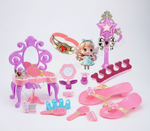 A pink and purple doll vanity playset with accessories including a vanity table, mirror, wand, tiara, sandals, brushes, and a small doll figure, arranged on a white background.