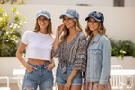 Three women wearing matching denim hats outdoors.