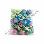 A clear plastic bag filled with assorted dog toys, including knotted rope toys, tug toys, and tennis ball toys in green, blue, pink, and yellow, photographed on a concrete floor.
