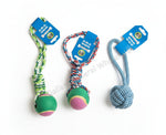 Three dog toys with blue tags are laid out on a concrete floor. The left toy is green and yellow rope with a green, pink, and yellow ball.
