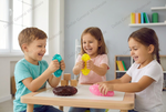 Three children sitting around a small wooden table in a bright room, squeezing colorful stress balls and handling textured toys. The scene includes visible Dallas General Wholesale watermarks across the photo.