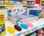 A retail display box of stress relief squeeze toys on a store shelf, with several colorful textured toys placed in front. Visible packaging includes LEGO and LEGO City boxes in the background, and the main product branding reads 'STRESS RELIEF SQUEEZE TOY'.