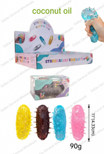 Coconut oil stress relief squeeze toy set shown with its retail display box, a smaller product box, four textured coconut-shaped toys in yellow, dark brown, blue, and pink, a hand holding a blue toy, and printed dimensions/weight text on a white background.