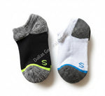 Two socks, one black and gray with green accents and the other white with blue accents, on a concrete surface.