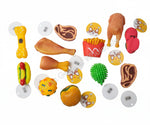 A collection of colorful novelty dog toys shaped like fast food items (burgers, chicken leg, hot dog, bone, fries, steak) and accessories, arranged on a gray concrete floor with their white circular retail tags visible.