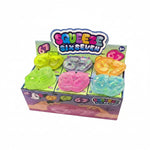 A retail display box of Squeeze Six Seven '67' squeeze toys, showing six translucent, glittery number 67 shapes in lime green, purple, pink, and blue, with a colorful 'SQUEEZE SIX SEVEN 67' sign behind them.
