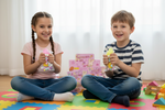 Two children sitting on a colorful mat playing with toys indoors.