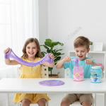 Two children sitting at a white table in a bright room, playing with colorful slime. The girl on the left holds up a stretchy purple slime, while the boy on the right scoops pink slime from a jar.