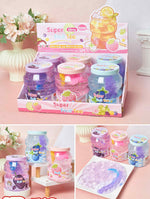 A retail display box filled with small jars of colorful slime, shown in a clean studio-style setup with decorative flowers and a white pedestal. The product packaging reads 'Super Mint Tea' and the jars contain pastel purple, pink, blue, and lavender slime.
