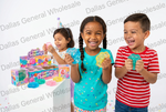Three children are smiling and playing with colorful Super Squishy squishy toys, with product boxes displayed on a table in the background against a white studio backdrop.