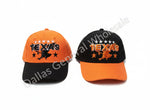 Two baseball caps with Texas-themed graphics, one orange and black and one black and orange, displayed on a concrete floor in a store aisle.