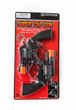 A toy 'Super Cap Gun' packaged in a red blister card on a gray concrete floor. The toy is a black replica of a revolver with bright orange safety caps on the barrels.