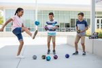 Three children playing with colorful patterned soccer balls on a concrete patio in front of a modern glass building. A semi-transparent 'Dallas General Wholesale' watermark is visible across the center.